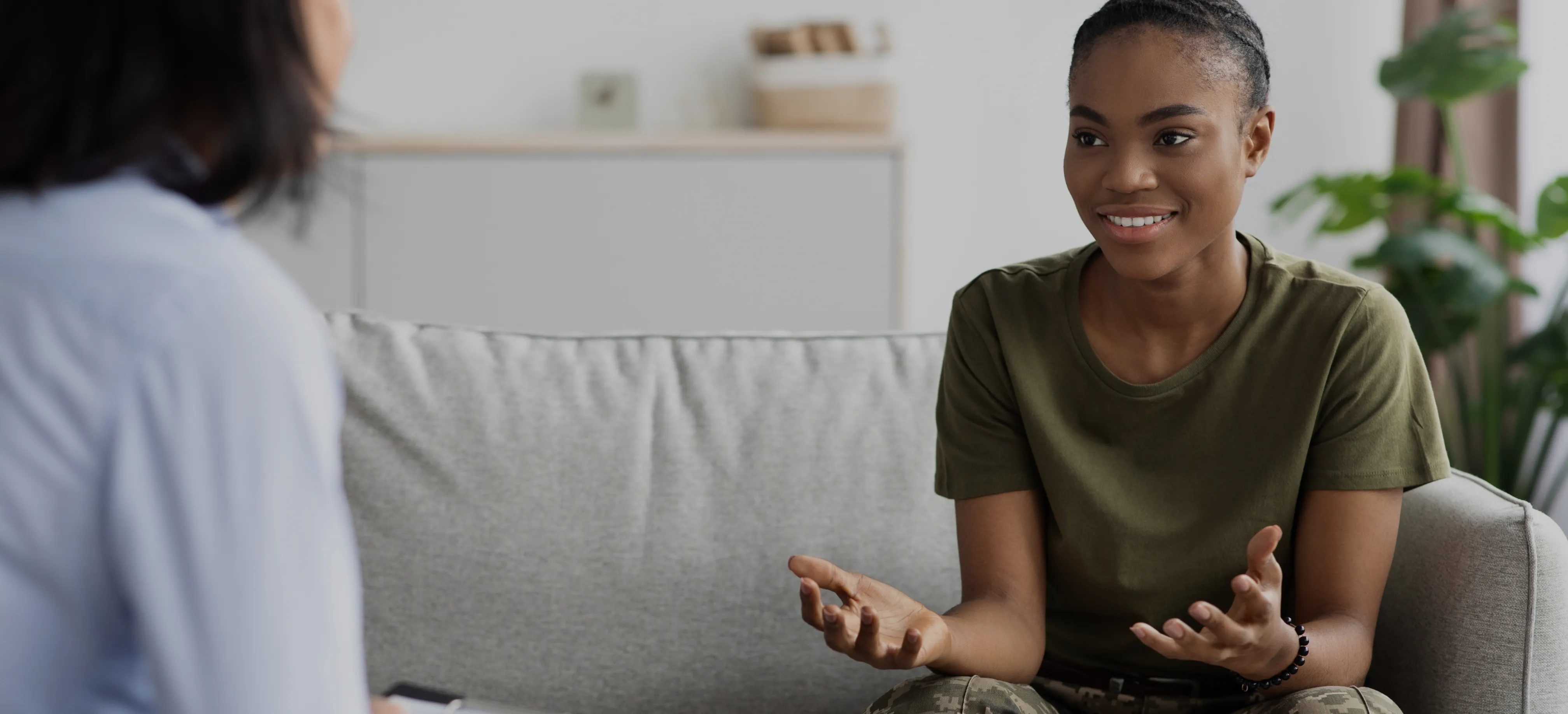 Two women talking to each other while sitting on a couch.