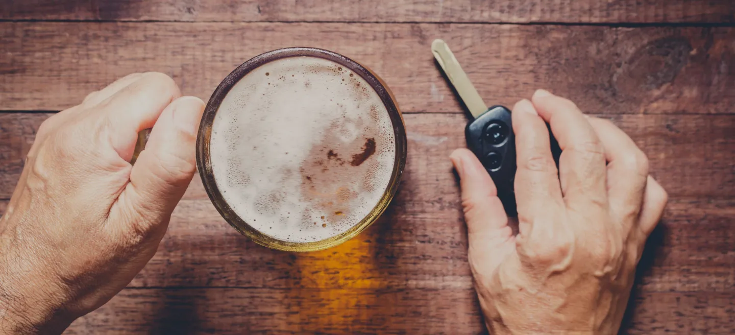 Top down view of a glass of beer in one hand and car keys in the other hand