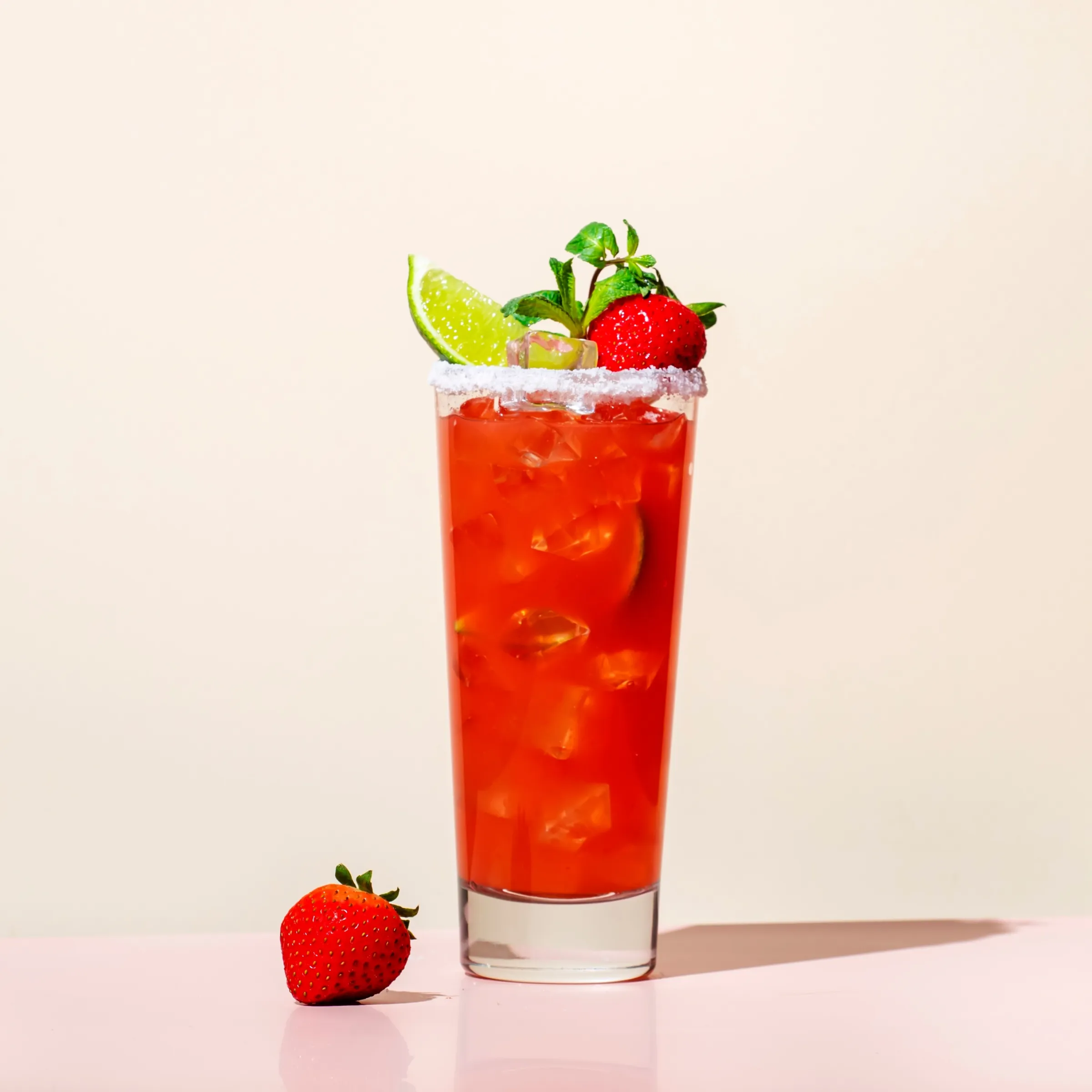 Deep red virgin cocktail in a tall glass filled with ice. Served with berries, lime and a salted rim.