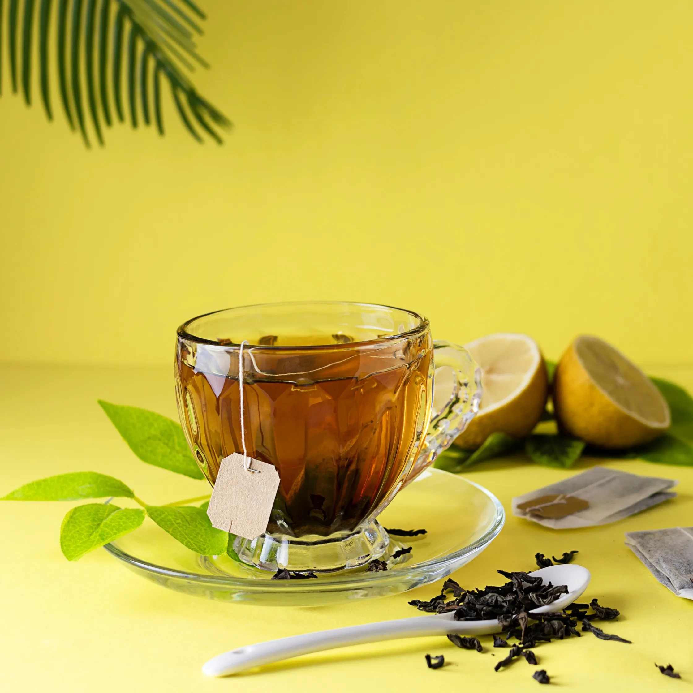 A brown mocktail in a transparent tea cup. A tea bag sits in the drink with various tea leaves nearby.