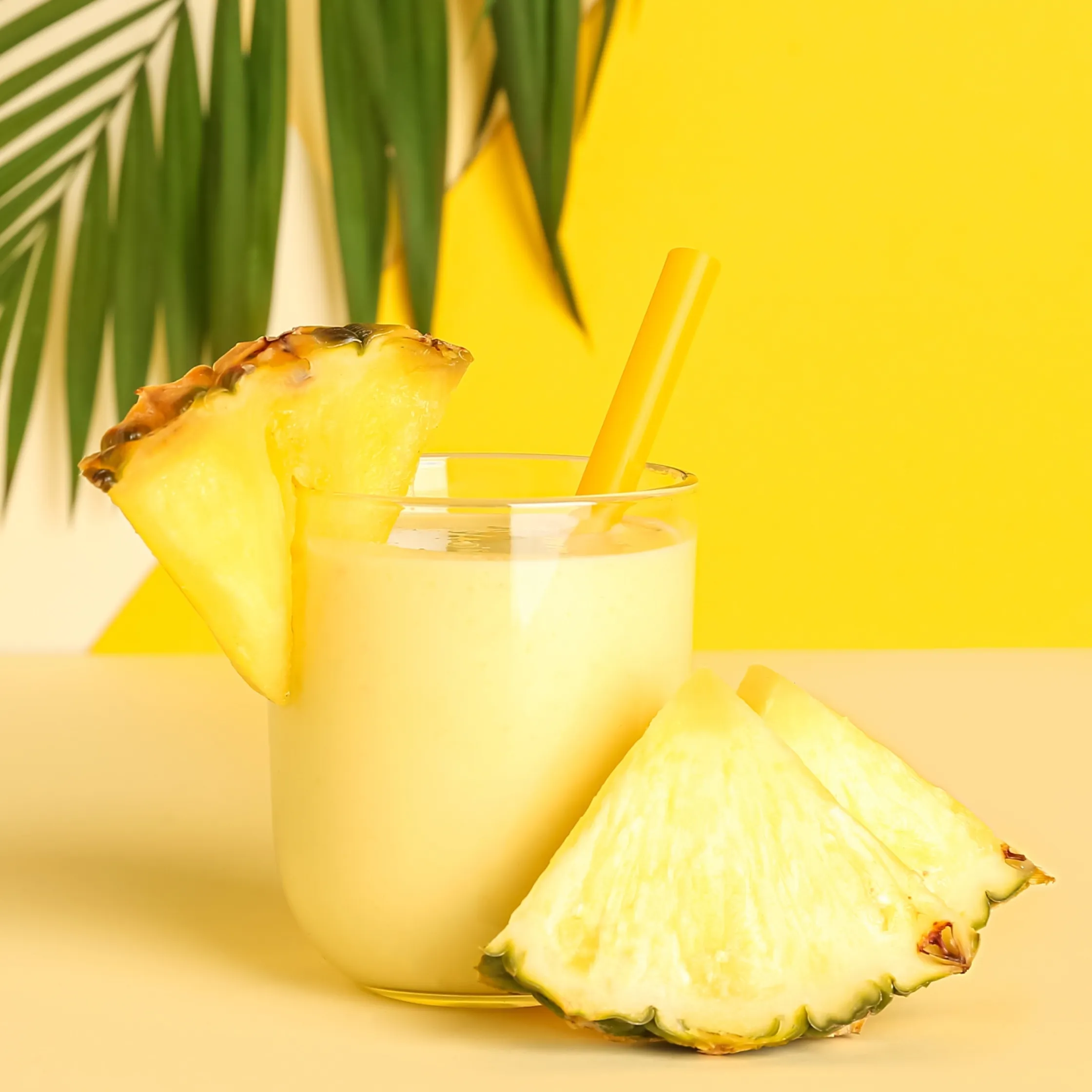 A vibrant light yellow zero-proof beverage with a thicker texture served with wedges of pineapple.