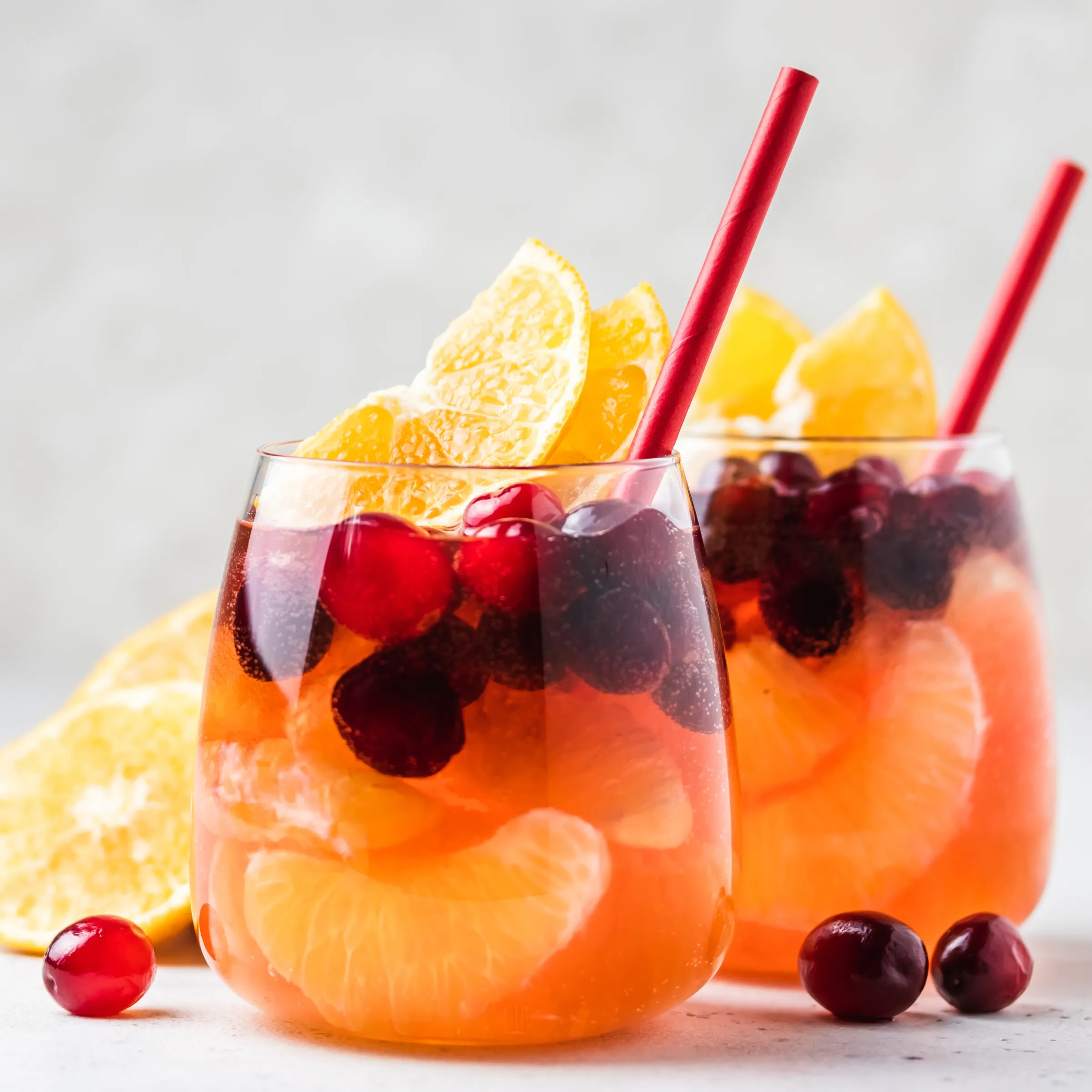 Stemless wine glass filled with a bright orange zero-proof cocktail. Mixed in with berries and orange slices.